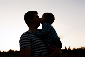 Father and his little son playing outdoors. Boy kisses his dad