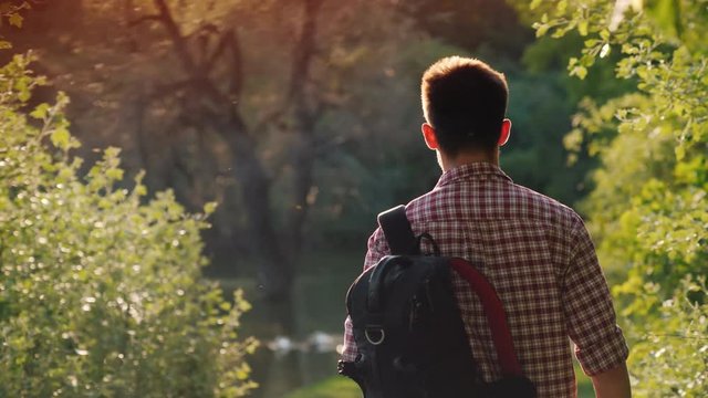 A teenager with a backpack walks through the park, the sun shines into the camera, beautiful glare
