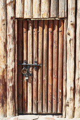 An ancient wooden door in a wooden wall. The door is closed with an iron latch and a lock