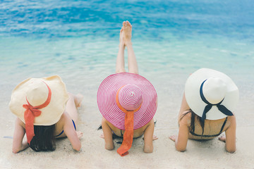 Three pretty beautiful asian woman wearing colourful swimwear bikini with hat living relax sunbathing on the beach in the summer