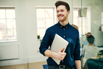 Smiling young businessman carrying a laptop in an office
