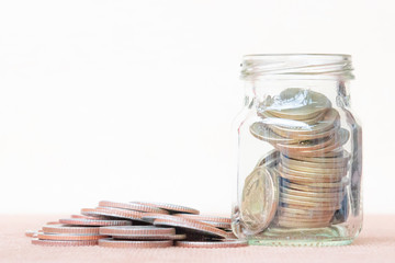Glass of coin and spread coin on floor on vintage blurred background - Saving money concept.