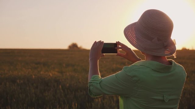 A woman in a hat takes pictures of a beautiful sunset over the wheat field