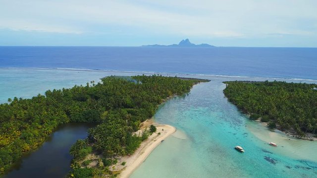 Aerial view of Motu Tautau, palm trees on little islets and clear blue lagoon, coral reef and Bora Bora on background, tropical paradise of Pacific Ocean - Tahaa island, landscape of French Polynesia