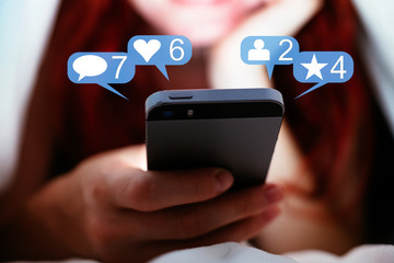 Woman with red long hair is using a smartphone with social media bubbles that indicate likes, articles, friends and comments
