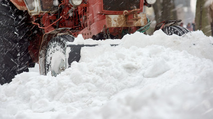 Closeup of red grader cleaning snow covered road after blizzard