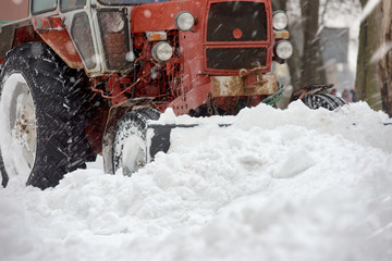 Closeup of red grader cleaning snow covered road after blizzard