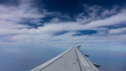 Fototapeta na wymiar Plane wing on blue cloudy sky background