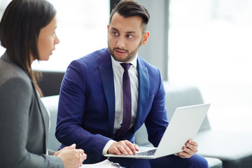 Fototapeta premium Young businessman with laptop looking at colleague while making presentation or discussing online data