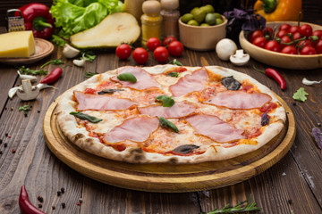Delicious italian pizza with ham and basil leaves on wooden background