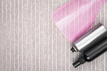 two bottles of professional hair sprays lying near a pink protecting shield for bang on a grey striped background. concept of hairdresser tools. free space for advertising