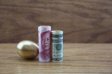 Gold nest egg with Chinese and American currency against wood background