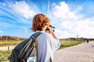 Young woman photographer traveler with a backpack doing a photograph of the landscape in a sunny summer beautiful day