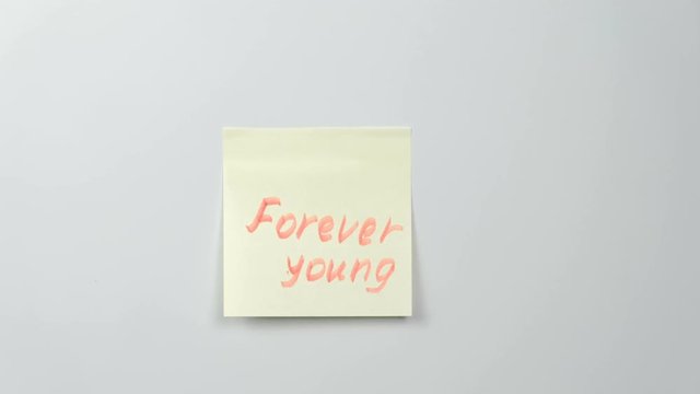 Closeup woman's hands stick yellow sticker paper sheets with words forever young.