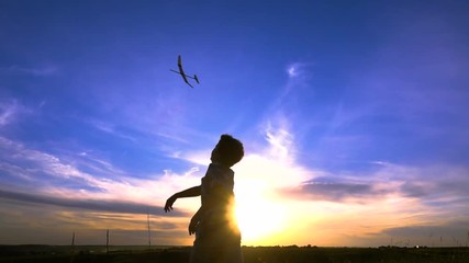 Silhouette of boy launching his airplanes against sunset