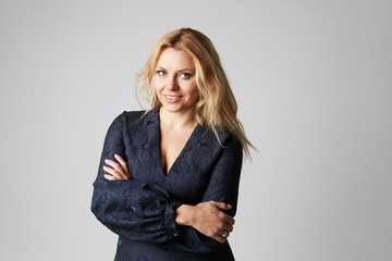 Fashion photo of a beautiful blonde woman in a pretty dress posing over gray empty background. Fashionable photo shot