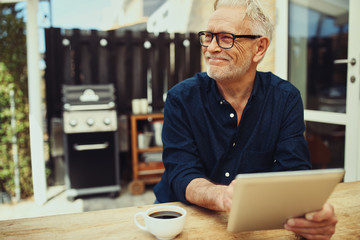 Smiling senior man sitting outside with a coffee and tablet