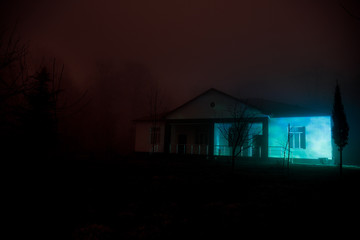 Old house with a Ghost in the forest at night or Abandoned Haunted Horror House in fog. Old mystic building in dead tree forest. Creepy house in the middle of a dark forest.
