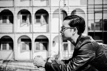 Handsome cool guy is thinking something. Attractive handsome man looks depressed and stressed. He stands in overpass and looks something. Glamour man wears sunglasses, jacket with building background