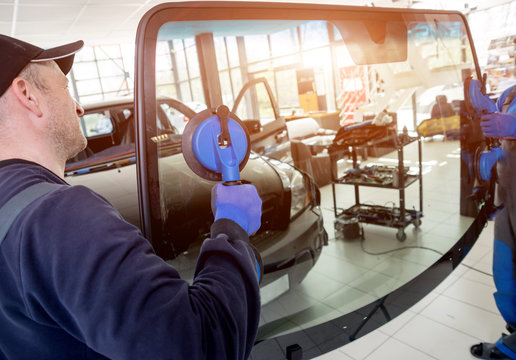 Automobile special workers replacing windscreen or windshield of a car in auto service station garage.