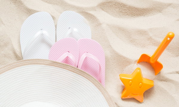 Beach hat and flip flop. Bright plastic children's toys on the sand. The concept of a beach holiday for children. Summer concept. Flat lay, top view, copy space 