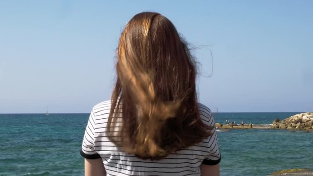 Girl with long red hair in the beach, sea breeze play with hair, daytime shot in Tel Aviv.