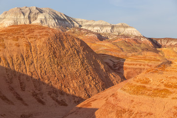 Multicolored red, orange and yellow striped hills with creek bed under a bright blue sky in Eastern Kazakhstan