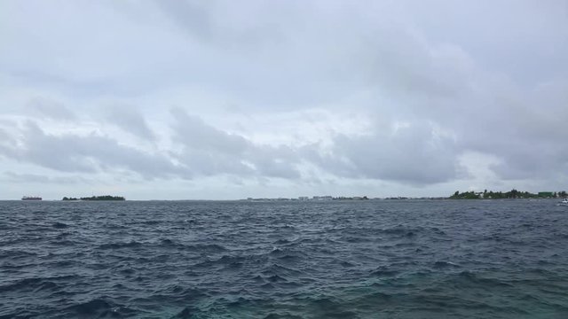 Beautiful view of dark blue water of Indian Ocean. White speedboat is passing by. Horizon line and white clouds on blue sky background. Malé, Maldives.
