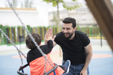little boy having fun swinging at the park, hi five with his father
