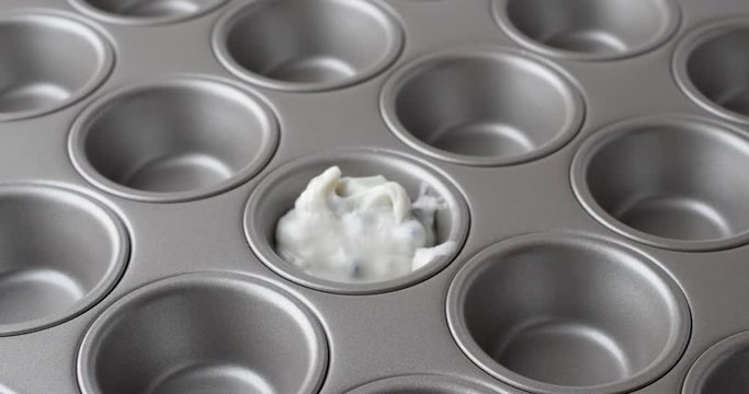 Close view of blueberry muffin batter being spooned into a mini muffin baking pan.
