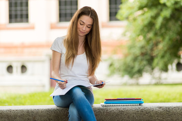 Beautiful female college student reading a book on a bench in a park
