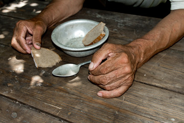Hands the poor old man's, piece of bread and empty bowl on wood background. The concept of hunger...