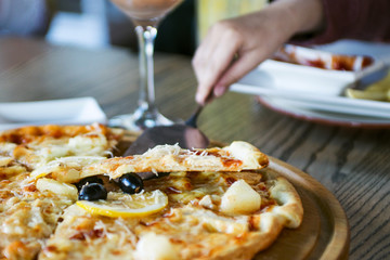 Man hand taking slice of pizza from wooden board. People eat fast food in cafe