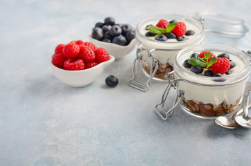 Yogurt parfait with homemade granola and fresh berries in a glass jars on blue concrete background, healthy breakfast concept, selective focus, copy space.