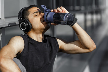 Attractive young dark skinned sportsman with short beard drinking water from bottle