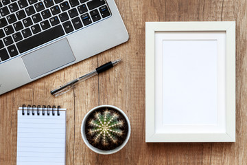 A brown wooden desk with a laptop, a cactus and a white empty frame