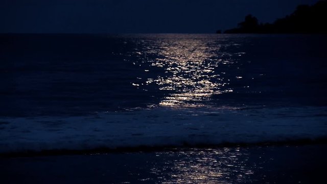 Full moon reflection on a Caribbean Beach.  White wake on the waves of the sea in the tropics. Waves breaking on the shore in the light of the moon.
