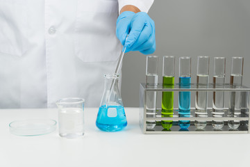 laboratory scene, the scientist holding the glass stirring rod. test tubes in the rack. flask, watch glass and beaker on the table
