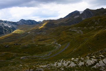 A twisted mountain road leading through rocky meadows and hills  