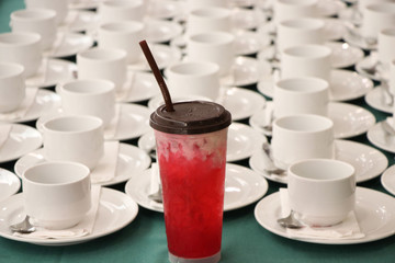 The empty white cups with spoons put on table waiting guests on the table Hotel  and red syrup in plastic glass with ice on table also