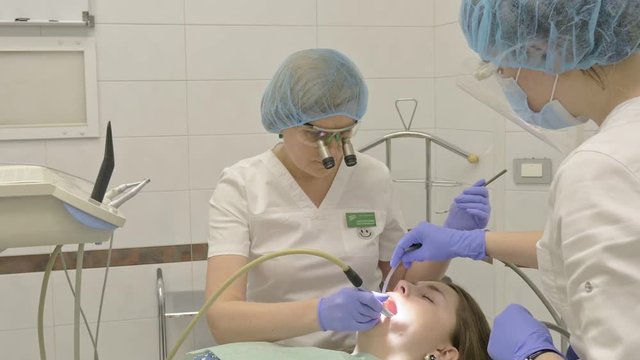 Woman at dentist clinic gets dental treatment to fill a cavity in a tooth. Dental restoration and composite material polymerization with UV light and laser. The doctor works with an assistant.