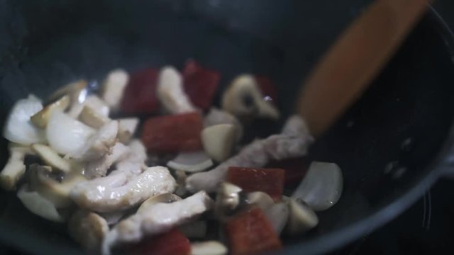 Mushrooms, onion and chicken being fried on a pan in a restaurant kitchen by a skilled cook. Handheld real time close up shot