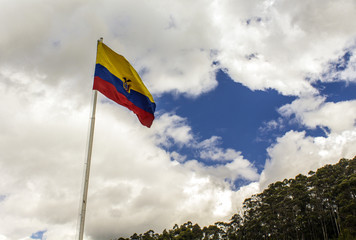 Flag of the Republic of Ecuador, on a sunny day with the city of Quito in the background.