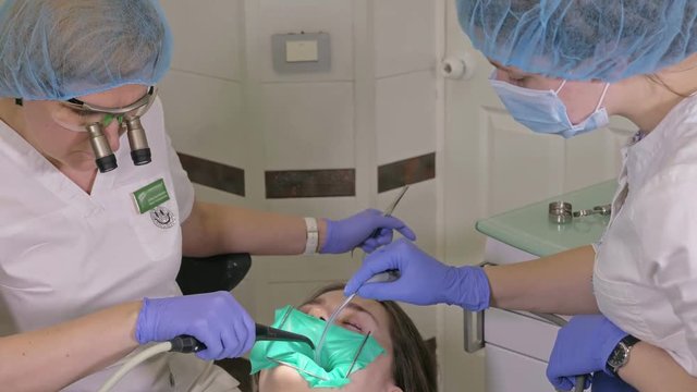 Woman at dentist clinic gets dental treatment to fill a cavity in a tooth. Dental restoration and composite material polymerization with UV light and laser. The doctor works with an assistant.