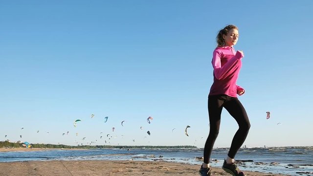 Woman running in summer on the beach on a background of kitesurfers at sunset, slow motion