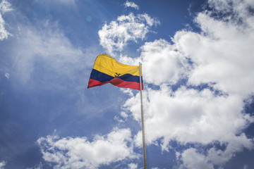 Flag of the Republic of Ecuador, on a sunny day with the city of Quito in the background.