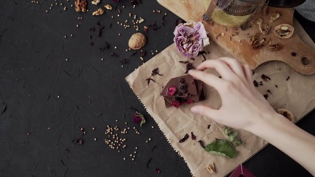 Flatlay on dark background with chocolate, walnut, wood board and paper. Womans hands prepare for photography.