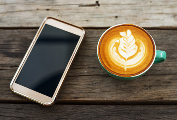Cappuccino coffee in a green cup with smartphone mobile on wooden