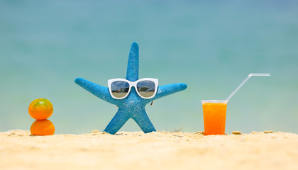 blue starfish, sunglasses and a drink on the beach sand