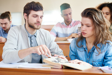 Two friends sitting at the same desk and discussing book together